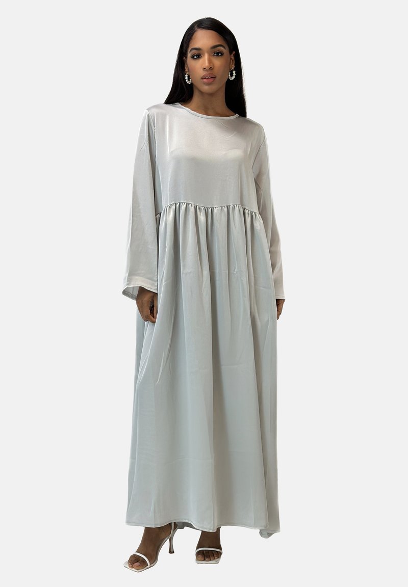 Robe longue en satin argenté avec un col rond, des manches longues et une taille froncée, donnant place à une jupe fluide. Portée avec des talons.
