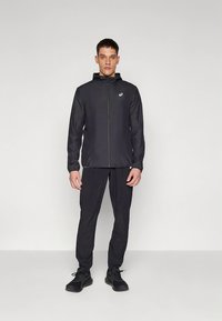 Zwarte lichtgewicht jas met ritssluiting aan de voorkant en verstelbare capuchon. Gecombineerd met bijpassende zwarte broek en sneakers, voor een samenhangende sportieve look.