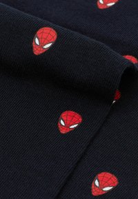 Svart stickad tyg med upprepade röda Spider-Man ansiktsloggor med vita ögon. Texturen är mjuk och elastisk, lämplig för avslappnad klädsel.