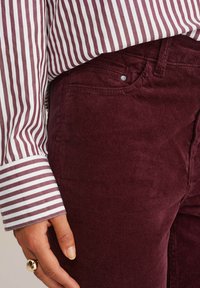 Burgundy kordbársony nadrág finom függőleges bordákkal, párosítva egy bordó és fehér csíkos inggel, amely kontrasztos mandzsettával rendelkezik.