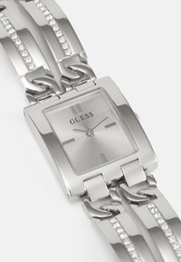 Silver rectangular watch with a brushed finish, linked bracelet featuring clear accents, and minimalistic dial marked with "GUESS."
