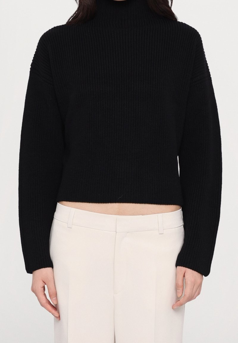 Sort, ribstrikket rullekravesweater med en kort silhuet og brede ærmer, kombineret med beige bukser med en glat tekstur.