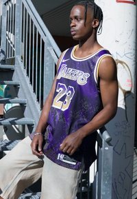 Maglietta da basket viola con la scritta "Lakers" e il numero "23", caratterizzata da un motivo a punti sfumati, indossata sopra pantaloni beige larghi.