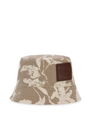 Chapeau bob beige et blanc à motif floral avec une étiquette en cuir marron embossée "GUESS EST. 1981" sur le devant.