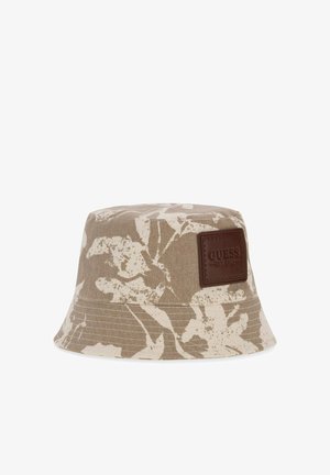 Chapeau bob beige et blanc à motif floral avec une étiquette en cuir marron embossée "GUESS EST. 1981" sur le devant.