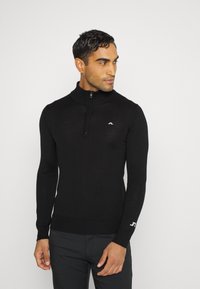 Black zip-up sweater with a high collar, made from a smooth knit material, featuring a small logo on the chest and ribbed cuffs.