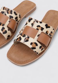 Sandalias de slide con estampado de leopardo, correas de cuero marrón, suela plana y una textura suave. Presenta un diseño cruzado y una plantilla en colores neutros.