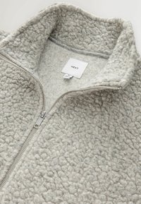 Gray fleece jacket with a high collar, featuring a smooth zipper and a textured surface. Label reads "NEXT."