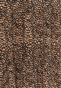 Svart tyg med ett spritt oregelbundet beige prickmönster och en subtil rynkad textur som bildar vertikala veck.