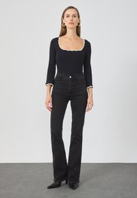 Svart langermet body med hvit bølget halslinje, kombinert med høyhårede svarte jeans. Skoene er spisse svarte hæler.