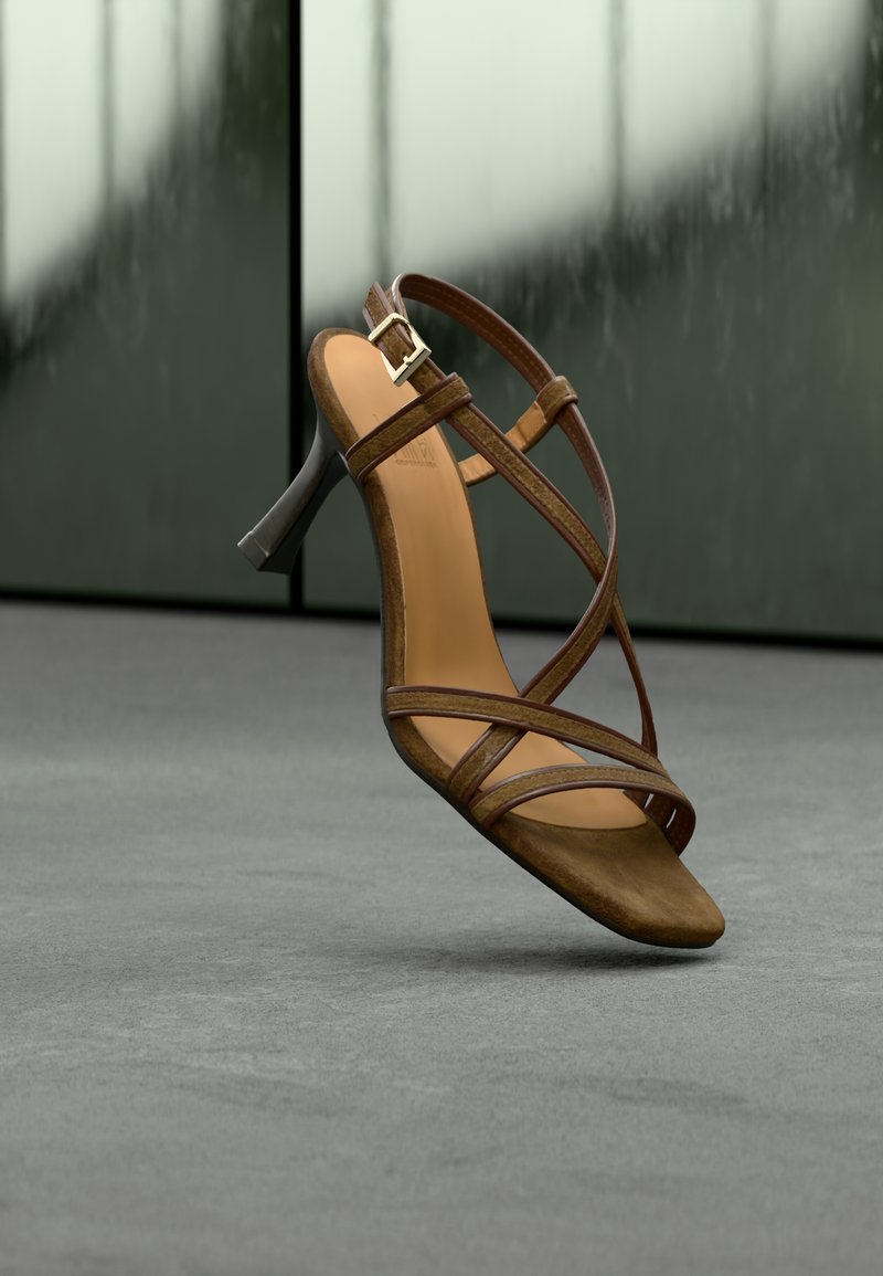 Καφέ δερμάτινο πέδιλο με λουράκια και τακούνι, με λεία υφή, σχέδιο ανοιχτών δαχτύλων, αγκράφα στον αστράγαλο και κομψό μαύρο τακούνι σε μια μινιμάλ φόντο.