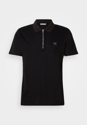 Musta polo-paita, jossa on lyhyt vetoketjukaulus, puuvillakangasta, pieni logo-ompelu rinnassa ja lyhyet hihat.
