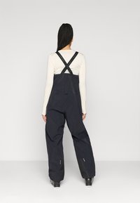 Μαύρες αδιάβροχες σαλοπέτες με ρυθμιζόμενους ιμάντες ώμου και άνετη εφαρμογή, οι οποίες διαθέτουν τσέπες με φερμουάρ και ενισχυμένα κάτω πόδια.