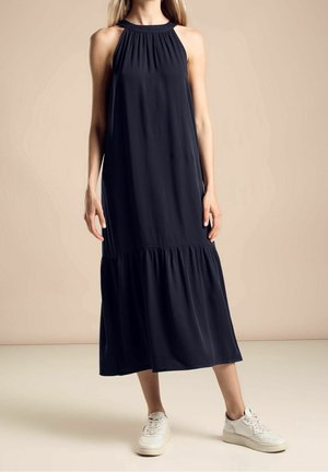 Marineblauwe maxi-jurk met een halterhalslijn, geplooide lijfje en een volant zoom. Gecombineerd met witte sneakers. Gladde stof, losse pasvorm, enkellengte.