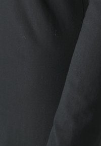 Schwarzer Stoff mit einer glatten, matten Textur; das Material wirkt weich und leicht dehnbar, wobei subtile Farbvariationen sichtbar sind.