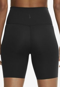 Vue arrière d'une personne portant un short de sport noir taille haute avec un petit logo Nike sur la ceinture.