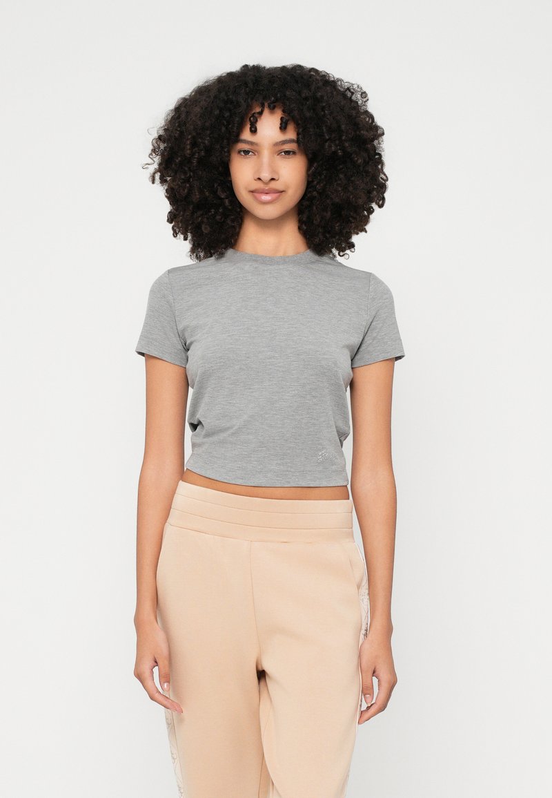 Maglietta grigia a maniche corte, con una leggera trama e scollo rotondo, abbinata a pantaloni della tuta beige con accenti laterali.