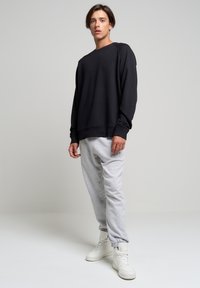 Čierna mikina s uvoľneným strihom, skombinovaná so svetlo šedými teplákmi. Model má na sebe biele high-top tenisky. Jednoduchý dizajn, bez vzorov.