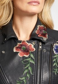 Czarna skórzana kurtka motocyklowa z kolorowym haftem kwiatowym w czerwieni i błękicie, z klasycznym kołnierzem i srebrnym zamkiem błyskawicznym.