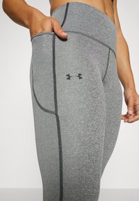 Szare legginsy sportowe z kieszenią w pasie, czarnymi wstawkami i małym czarnym logo na udzie. Gładki, elastyczny materiał.