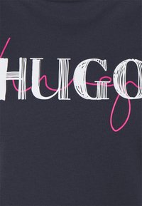 Námořnické bavlněné tričko s výrazným bílým a růžovým nápisem "HUGO", s vlnkovou linií propletenou mezi písmeny.