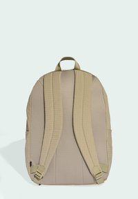 Beige backpack with padded mesh straps, textured fabric, and a top handle. Features side pockets and adjustable strap hardware.