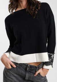 Maglione nero con orlo bianco. Presenta dettagli in pizzo ai polsini. Tessuto morbido e vestibilità comoda. Abbinato a jeans grigi a vita alta.