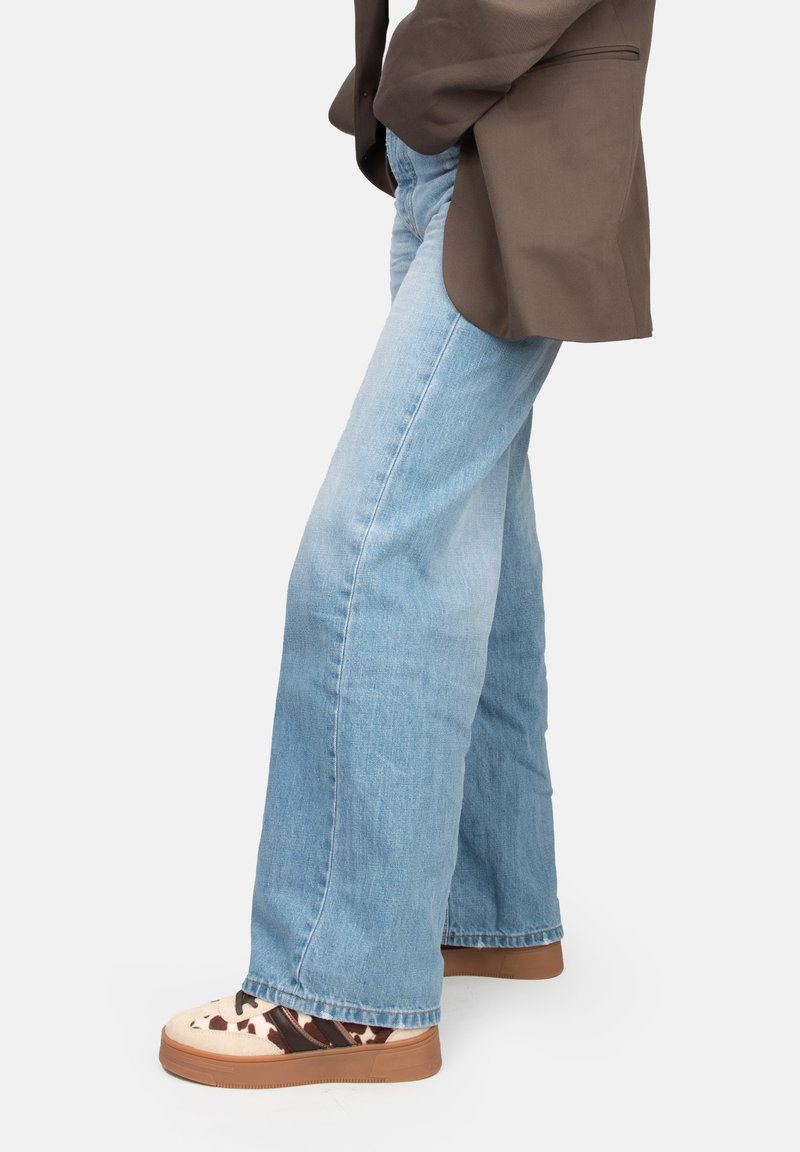 Vaqueros acampanados de color azul claro hechos de mezclilla, combinados con calzado de patrón beige y marrón que presenta un upper texturizado y suela de goma.