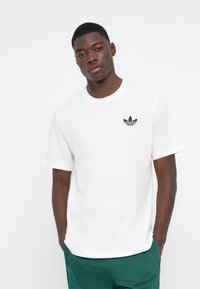 Hvid bomulds t-shirt med et lille sort Adidas trefoil-logo på venstre bryst, rund halsudskæring og korte ærmer.