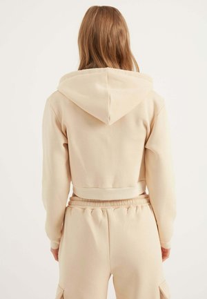 Lys beige cropped hoodie med snørredrens, blødt materiale og ribbede manchetter. Sammen med matchende højtaljede bukser.