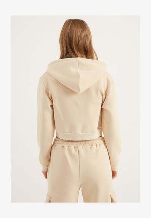 Lys beige cropped hoodie med snørredrens, blødt materiale og ribbede manchetter. Sammen med matchende højtaljede bukser.