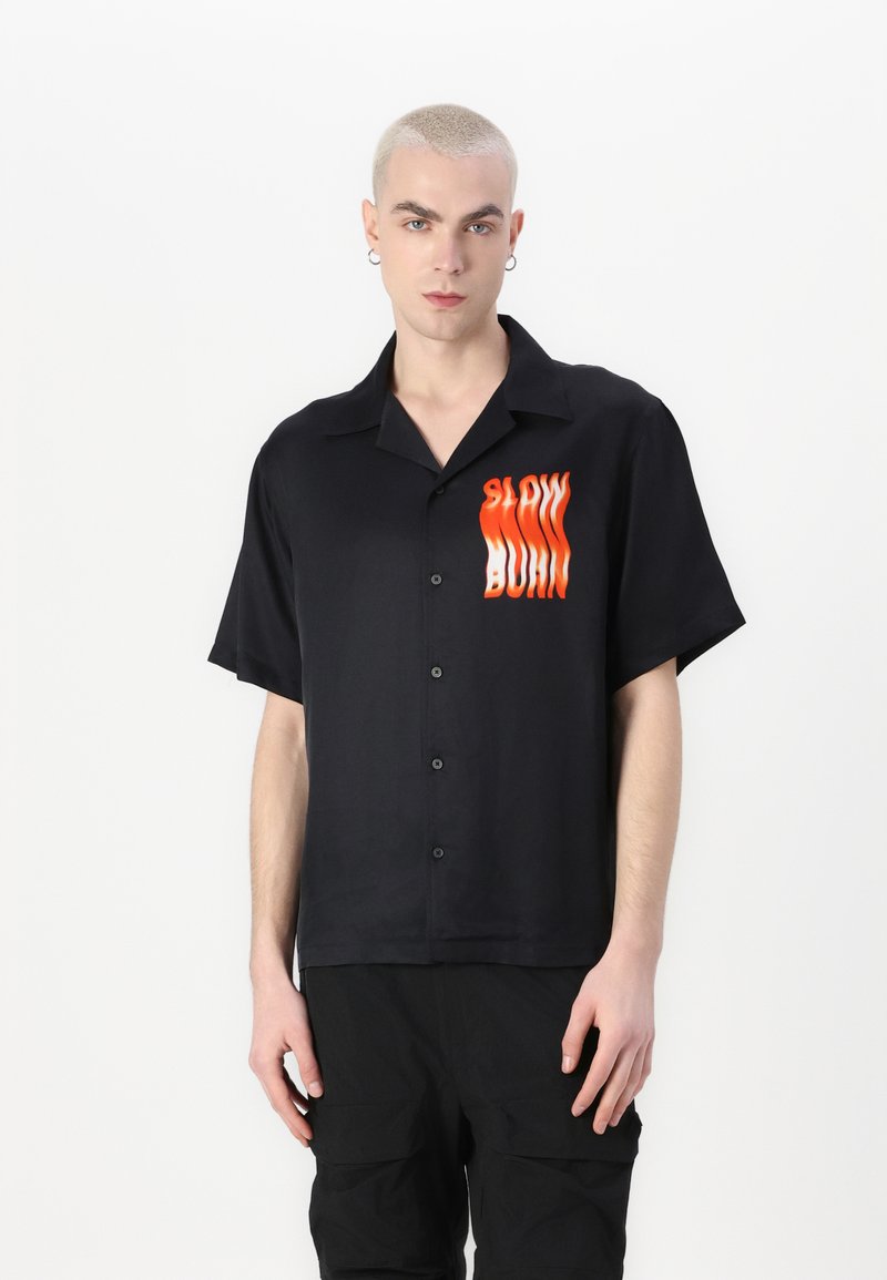 Zwart T-shirt met korte mouwen in een gladde stof, voorzien van een vooraanstaande graphic met de tekst "SLOW BURN" in oranje en rode golvende letters.
