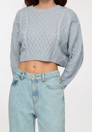 Pull court bleu clair en maille torsadée porté avec un jean taille haute délavé clair, laissant apparaître le ventre nu.