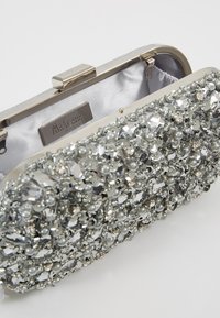 Srebrna torebka na łańcuszku z metalową ramą, ozdobiona kombinacją przezroczystych kamieni oraz pereł. Wnętrze wyłożone jasnoszarym satyną. Zapięcie u góry.