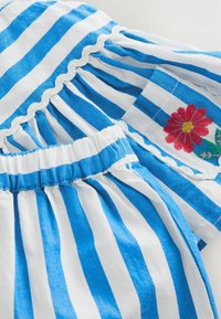 Blue and white striped fabric with scalloped edges and floral embroidery detail. Features soft texture and gathered elastic waistband.
