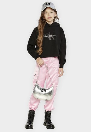 Felpa nera corta con logo "Calvin Klein Jeans", pantaloni cargo rosa in satin, borsa argentata e stivali neri con lacci. Indossato un cappellino grigio.