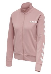 Veste légère rose pâle zippée avec col montant, motifs chevrons blancs sur les manches et logo "HUMMEL" sur la poitrine gauche.