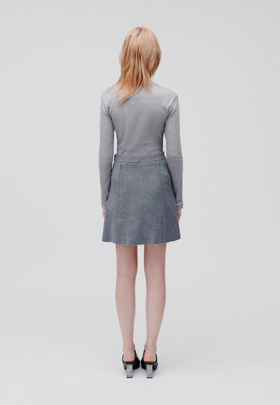 Grijze langemouwen shirt gecombineerd met een geribbelde grijze rok. De rok is uitlopend aan de onderkant. Zwarte hakken maken de outfit compleet.