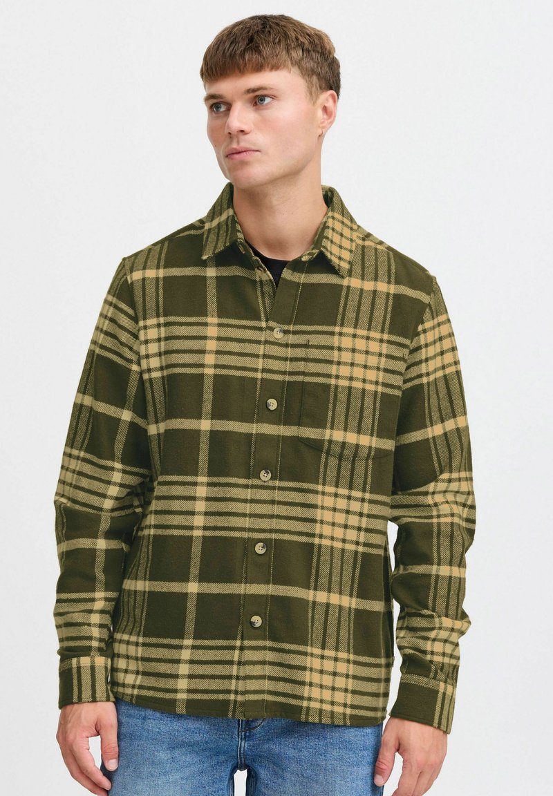 Chemise en flanelle à carreaux verts et beiges avec un bouton sur le devant, un col et des manches longues, fabriquée dans un tissu texturé. Elle dispose d'une poche poitrine.
