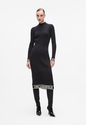 Black ribbed knit dress with a high neckline, long sleeves, and white "KARL LAGERFELD" logo accents at cuffs and hem. Fitted silhouette.