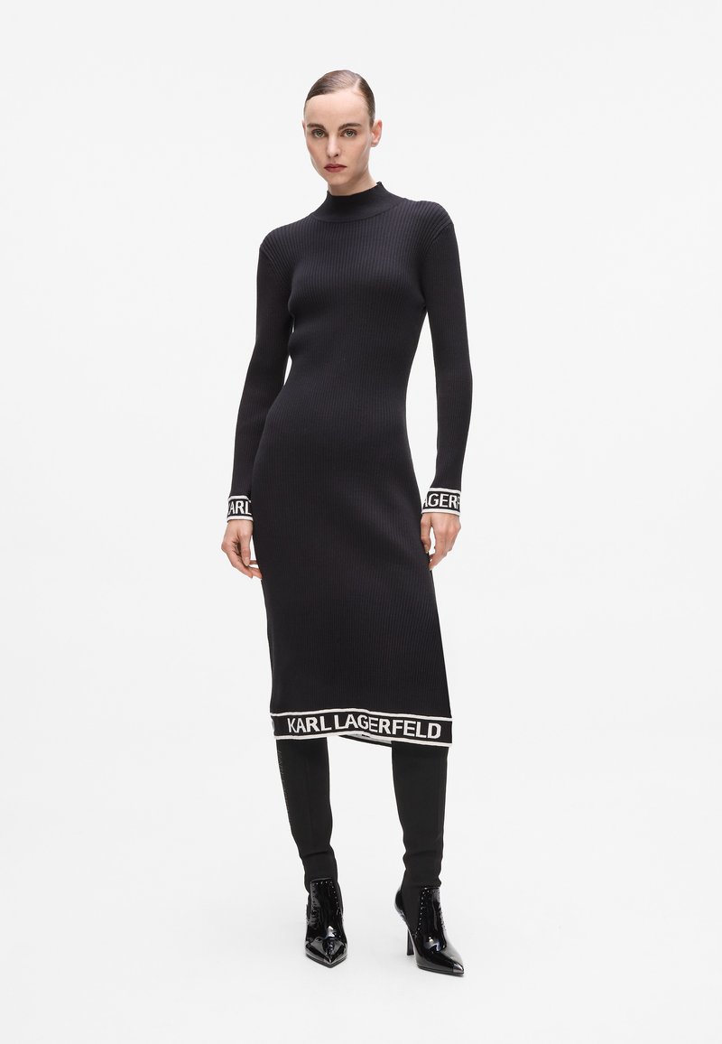Svart ribbad stickad klänning med hög halsringning, långa ärmar och vita detaljer med "KARL LAGERFELD"-logotyp vid ärmsluten och fållen. Figursydd silhuett.