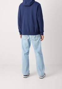 Marinblå hoodie med stor huva och ribbade muddara, tillsammans med ljusblå raka jeans. Avslappnade skor används.