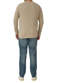 Beżowa koszula z długim rękawem i zaokrąglonym dekoltem, w połączeniu z wyblakłymi niebieskimi dżinsami. Koszula ma gładką teksturę i luźny fason.