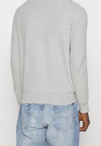 Grå stickad tröja med rund hals och ribbade muddar, ihop med ljusblå slitna denimjeans med synliga fickor och strukturerad yta.