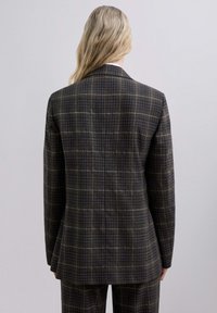 Blazer de cuadros marrón con una silueta ajustada, que presenta sutiles líneas azules y blancas. Textura suave con solapas estándar y abertura sencilla.
