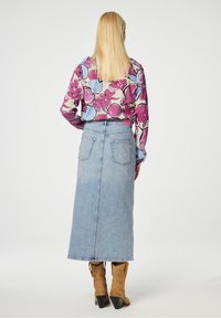 Langdenim rok met een lichte wassing, achterzakken en een hoge taille. Gepaard met een kleurrijke blouse met bloemenpatroon en tan laarzen.