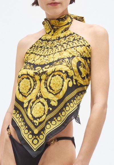 Črno-zlata svilena ruta z vzorci cvetličnih in baročnih motivov, ki ima trak za vezanje okoli vratu in lahkotno teksturo.
