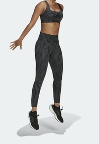 Zwarte sportbeha en strakke leggings met een subtiel tijgerstreep patroon. De outfit is gecombineerd met zwarte sportschoenen en toont actieve beweging.