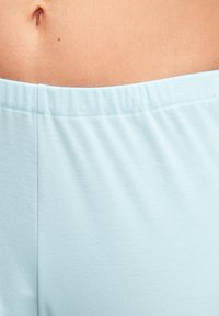 Lichtblauwe elastische tailleband met een zachte, gladde stoftextuur. Dichtbijzicht legt de kleur en stikseldetails extra in de verf.