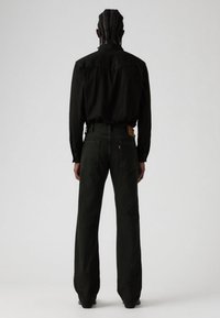 Zwart shirt met lange mouwen, achterkant zichtbaar, gecombineerd met donkergroene wijde jeans. Opvallende details zijn het Levi's-label op de achterzak.